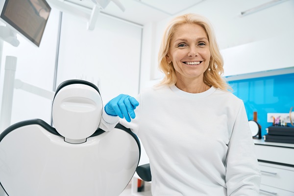 Smiling dental professional in a clinic, wearing gloves, beside a dental chair, promoting dental care services.