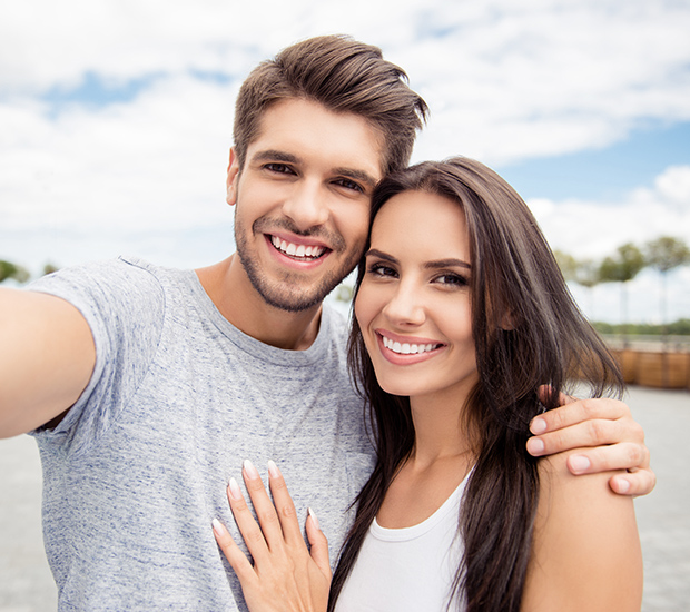Smiling couple taking a selfie, showcasing healthy teeth, reflecting confidence and happiness, relevant to dental implant candidacy discussions.