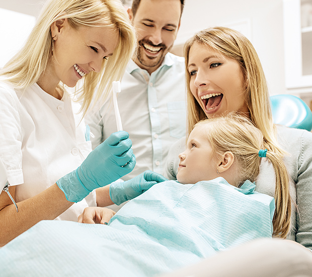 family-dentist Family dentist interaction with a child, showing a smiling dental hygienist holding a toothbrush, while parents express joy in a welcoming dental office setting.